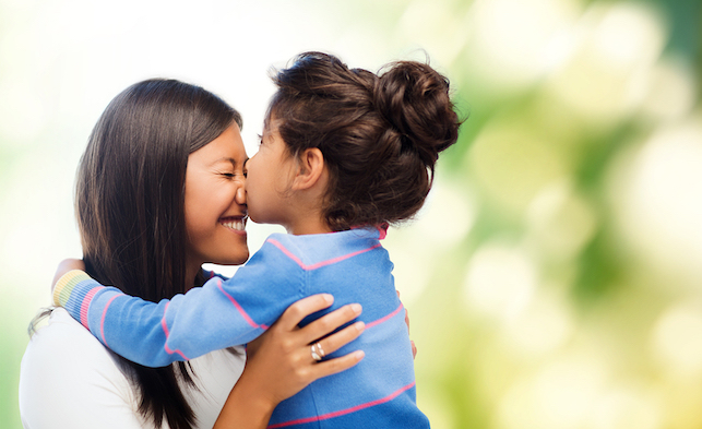 Young daughter kisses mom on the face in a joyful embrace