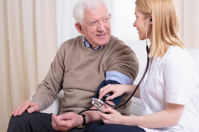 young smiling caregiver checando a hipertensão do paciente mais velho's hypertension