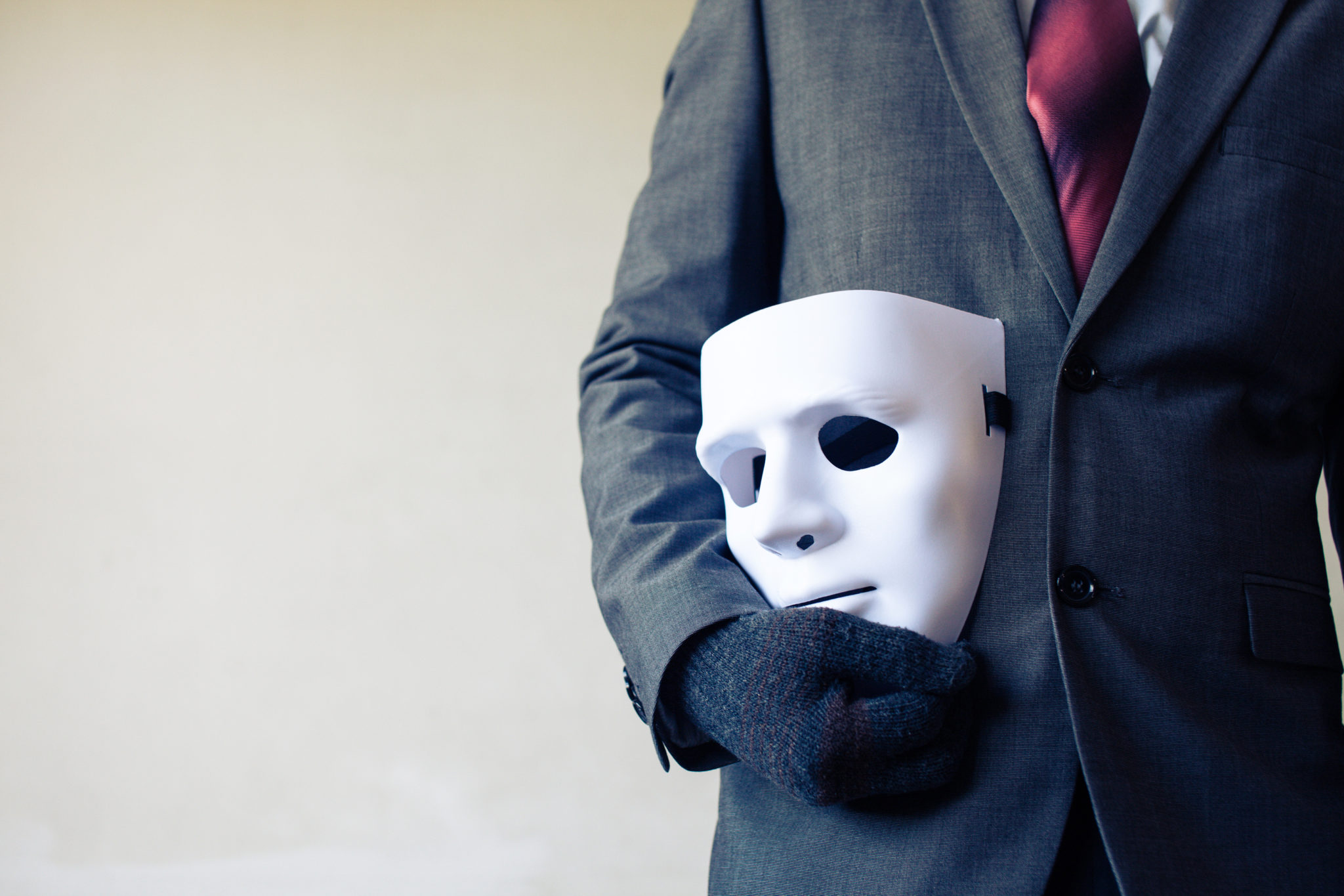 Man holding mask in business suit to defraud businesses