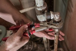 Plumber man replaces the tap in the bathroom. Fasten faucet using a wrench to rusty water pipe