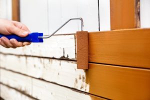 Man painted wooden boards with a bow roller and foam roller. Brown paint is painted or rolled on a wooden wall