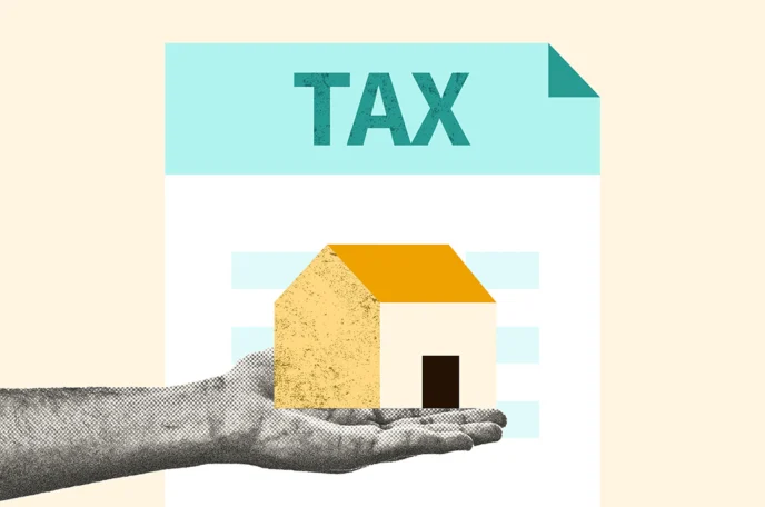 A hand holding a model home in front of a tax document to represent how an LLC can provide tax benefits for a rental property