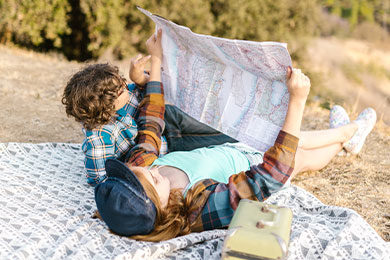 two kids lying down on picnic blanket while looking at a map
